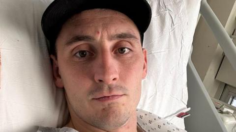 Sam Davies lying on a hospital bed 