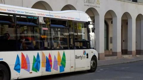 A single storey bus with colourful graphics on the site and lettering.