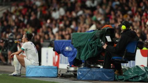 Lucy Bronze of England sits down with a drink during the game in front of a TV camera