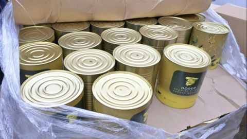 An open crate of gold food cans sits on a cardboard base. They have a yellow and green label on them.