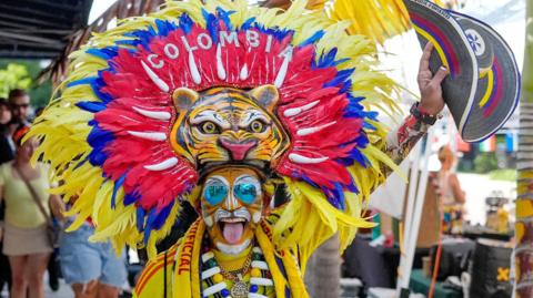A Colombia fan wears a tiger costume with bright headdress before watching their team play.