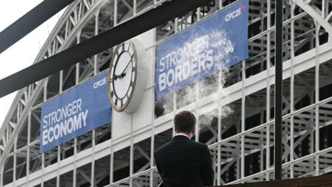 A man vapes into the air outside the venue on the third day of the annual Conservative Party conference in Manchester. He is standing in front of the former railway station and large blue banners saying Stronger Economy and Stronger Borders are hanging either side of the large station clock.  