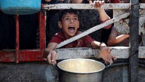 A Palestinian boy calls out while holding a pot waiting for food from a charity kitchen in Gaza City