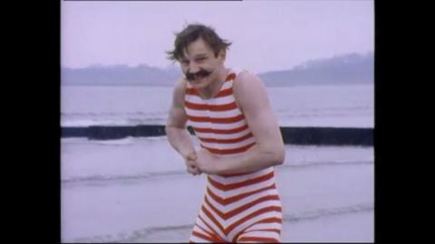 Liam Neeson dressed in a bathing suit at the sea.