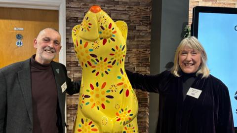 yellow rat statue with two people standing either side of it