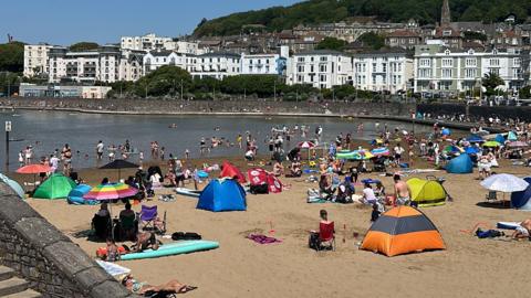 Many people are sitting on sand by a large marine lake in Weston-super-Mare.