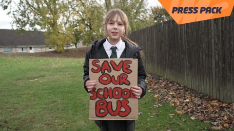 ella holding a sign that reads "save our school bus"