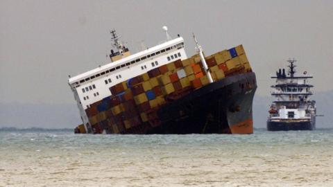 The Napoli lists heavily with containers on the deck and a tug off it's side
