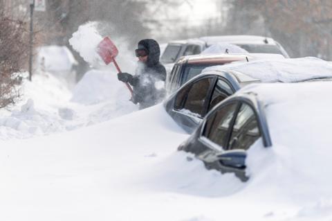 Four cars stuck in snow door height snow with a person with a shovel in black winter gear