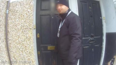 A person in a black jacket stands near a weathered black door.