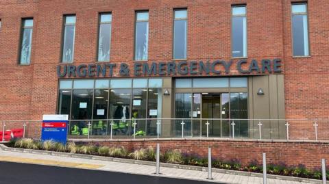 Exterior of red brick building with a sign over the glass doors reading Urgent and Emergency Care