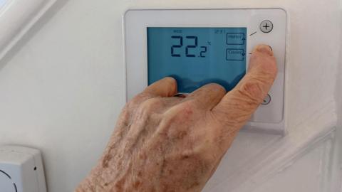 The hand of an elderly person is adjusting a smart meter on a household wall