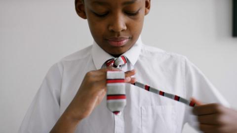A boy putting on school tie.