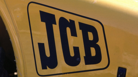 A close-up shot of a yellow vehicle, bearing three black letters spelling out JCB 