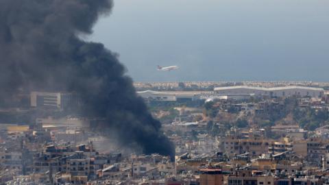 A plane takes off from Beirut's airport as smoke rises from the city's southern suburbs following an Israeli air strike (8 October 2024)