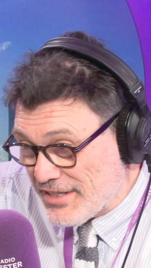 Andrew Russell speaking into a purple microphone. He is wearing headphones.