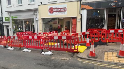 The front of a restaurant surrounded by red barriers and traffic cones