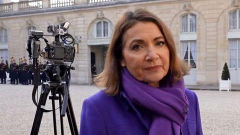 Katya Adler standing outside the Elysee palace in Paris. She is wearing a purple scarf and coat 