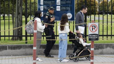A man and two women, one with a child in a pushchair, with a security official in the background, queuing for a visa at a US counsulate