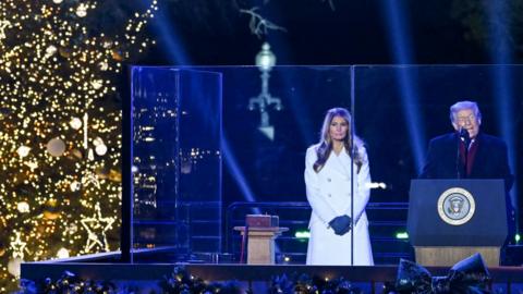 Melania Trump and Donald Trump are standing next to the National Christmas Tree.