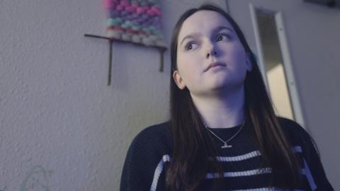 Megan mewn golygfa o'r ffilm Tyfu Mewn Galar - merch ifanc gyda gwallt hir tywyll mewn ystafell yn edrych tua'r pellter canolig