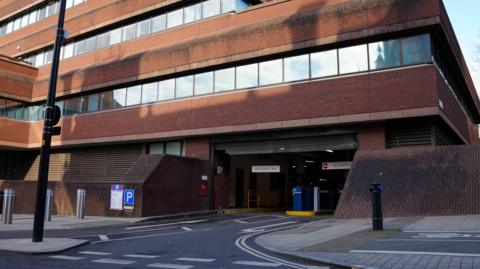 The entrance to an indoor car park. The building is red brick and the first, second and third floor have square windows. 