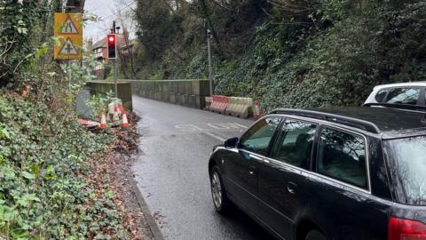 a car stopped at a red traffic light on the A29, with traffic cones and bollards on the road