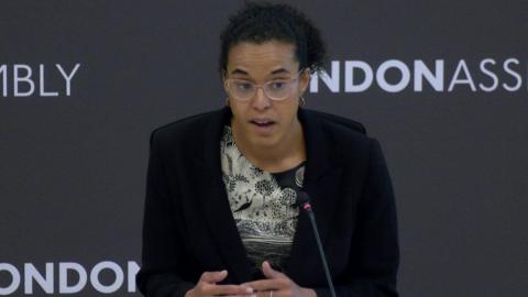 Kaya Comer-Schwartz, London's deputy mayor for policing and crime, speaking into a microphone at a London Assembly meeting. She has dark curly hair and glasses and is wearing a black blazer.