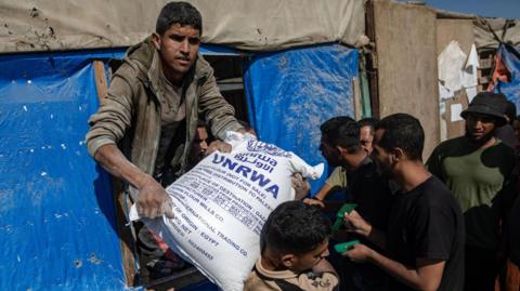 People distribute bags of flour to Palestinians at a United Nations Relief and Works Agency for Palestine Refugees in the Near East (UNRWA) aid distribution center in Khan Younis, southern Gaza Strip, 31 October 2024.