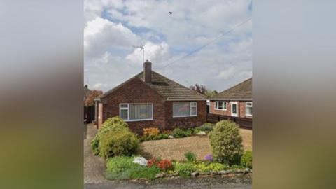 A brown-stoned modern bungalow with a garden in front. The garden has colourful flowers and a gravel drive. 
