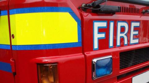 A close-up of the front of a fire engine - FIRE in large letters on red with yellow to one side.
