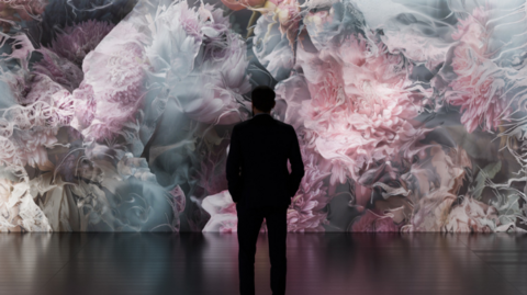 A silhouette of a man standing in front of a pink swirling light show on a wall in front of him.
