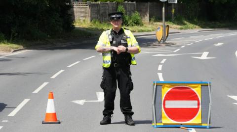 A police officer stood in the middle of a road, with a road closed sign next to him.
