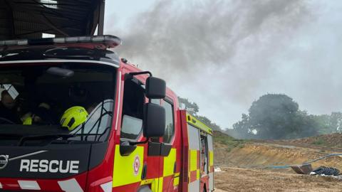 A fire engine with a plume of smoke billowing up behind