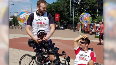 Two men pose with their bicycles after a race. One is in an adjusted bicycle for mobility issues