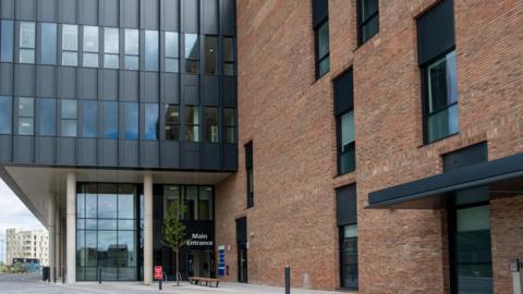 The glass main entrance to Sunderland's new eye hospital. The building has tall windows and is mostly made of brown bricks.