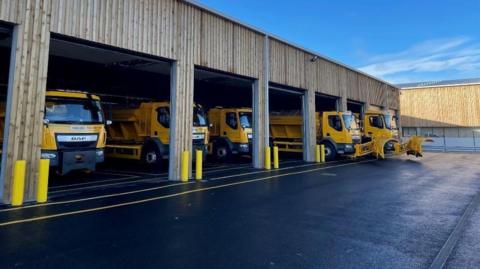 A view of Warminster salt depot with five yellow gritting vehicles parked at a holding station