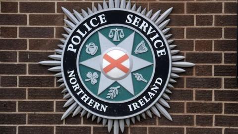 Police Service of Northern Ireland official crest is shown mounted outside on a brick wall.  