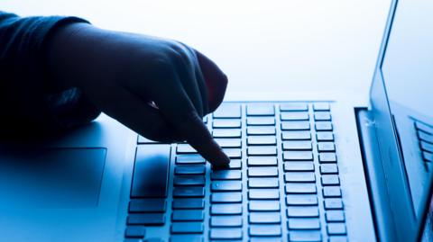 A hand covered in shadow rests a finger on a black computer keyboard.