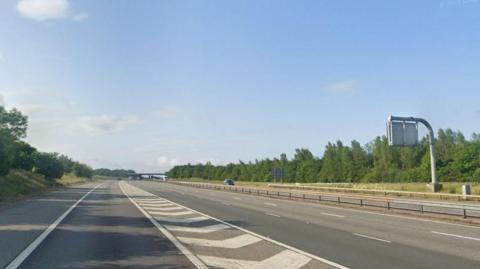A stretch of the M40 motorway. Barriers can be seen down the middle with trees on each side.