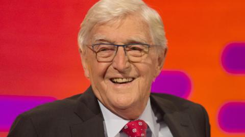 Sir Michael Parkinson during filming of the Graham Norton Show at The London Studios, south London, in 2016. He is smiling and is wearing a black jacket and red tie.