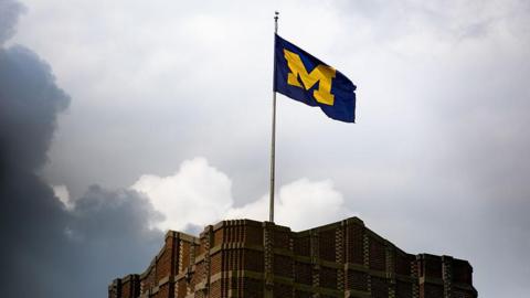 A large flag with the letter M in yellow against a blue background perched atop a building.