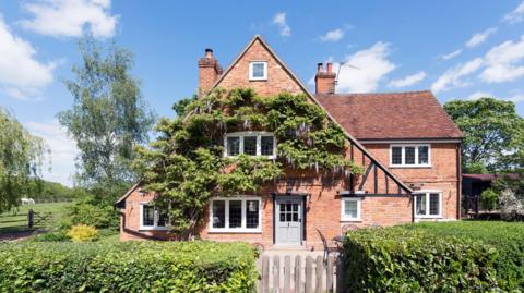 A large distinctive looking house in the country with a distinctive high ridge and a front which is covered in ivy
