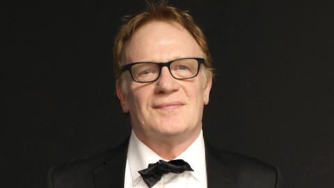 Llun o Mark Lewis Jones mewn tuxedo