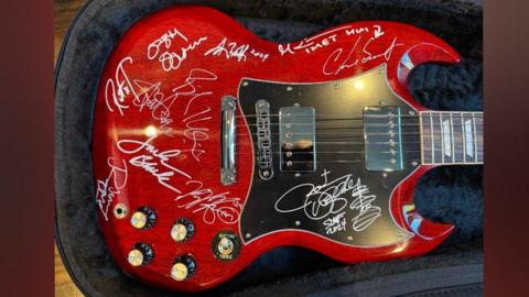 A red electric guitar that has been signed by several people, including Ozzy Osbourne in white marker