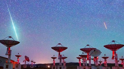 Blue and red shooting stars visible in the night sky above a number of large telescopes