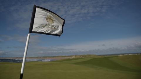 A Trump golf course flag sits in the green at the site in Doonbeg, County Clare. The fore is green with the beach and sea in the distance.