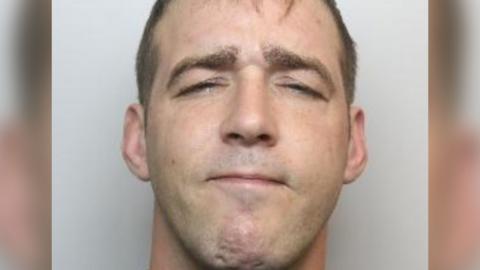 A police mugshot of Michael Stewart. He has short, dark hair.