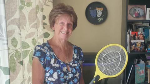 Lady with blue top and electric fly swatter in a house setting 