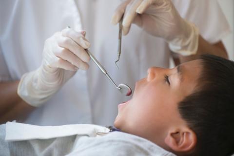 Side view of an open-mouthed young boy in a dental surgery with clinician using a mouth mirror to examine the child's teeth